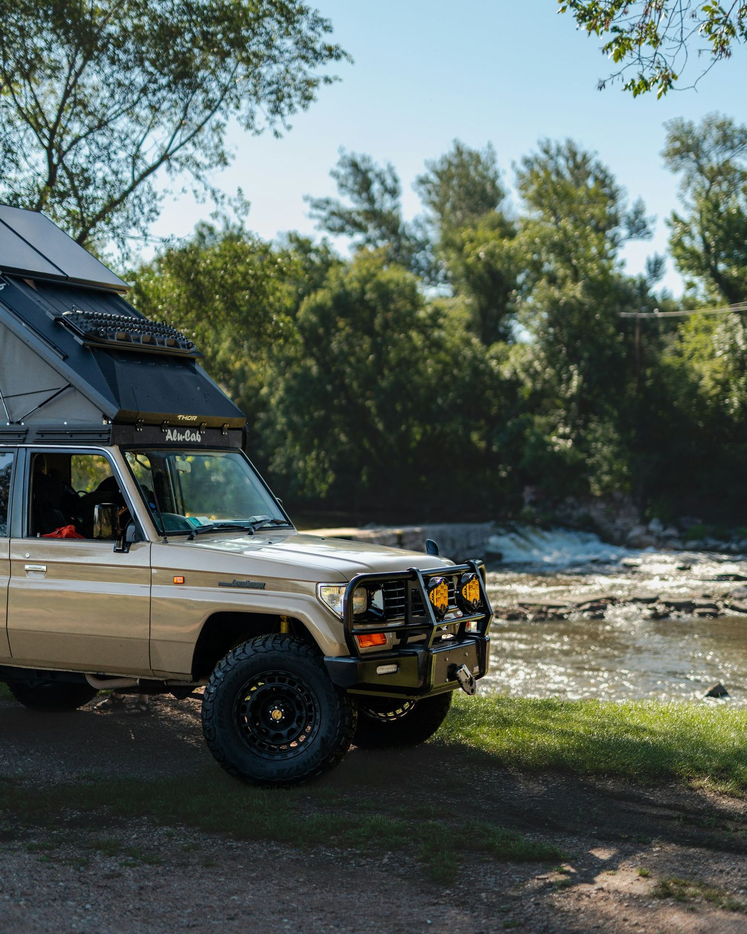 A rugged, modified vehicle camps by a river.